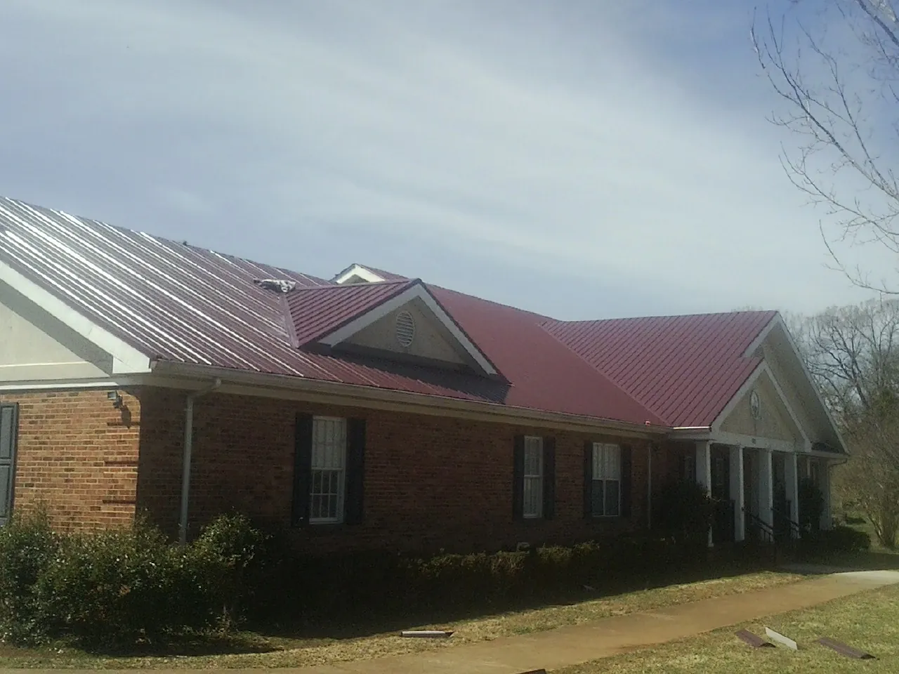 Red metal roof with gabled entries on a long brick building, from a Hail Damage Roof Repair job in Hysham