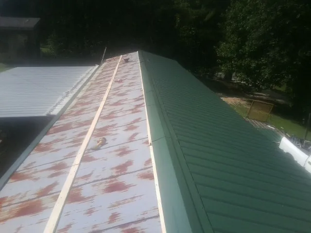 Old rusted panels beside newly installed green metal roofing — Wind Damage Roof Repair by Roofing Brothers in Hysham
