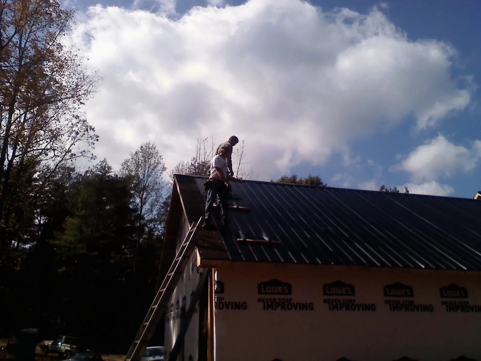 Roofer fastening dark metal panels high against a cloudy sky, from a Roof Inspection job in Hysham