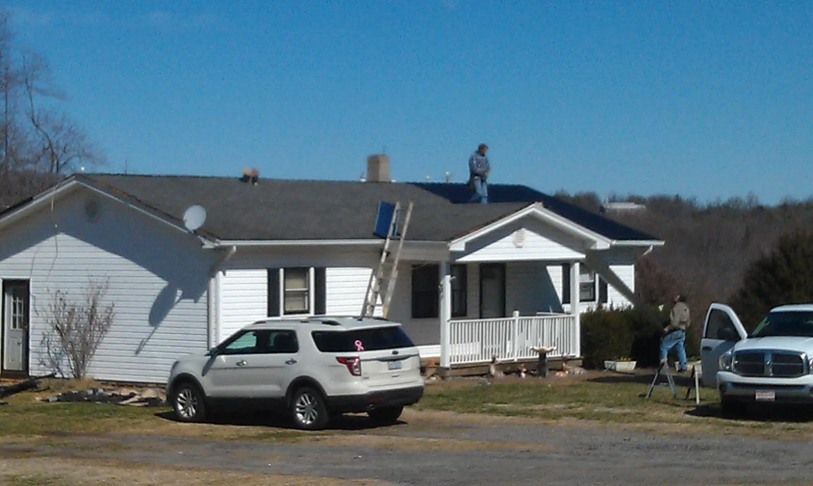 Roofers stripping shingles from a white ranch house roof in Hysham