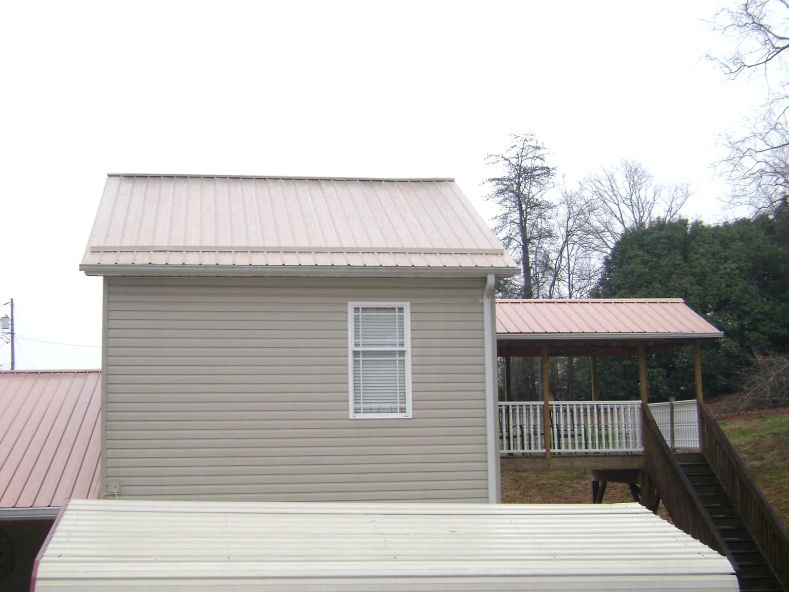 Tan metal roofs on a two story addition and attached porch, from a Roof Replacement job in Hysham